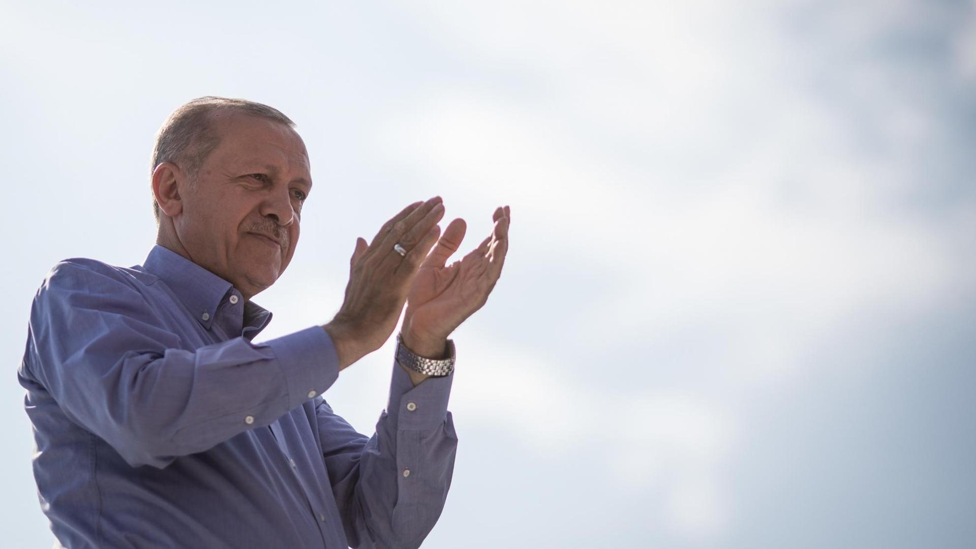 Der türkische Präsident Erdogan in blauen Hemd klatschend vor blau-weißem Himmel. Der türkische Präsident Erdogan in blauen Hemd klatschend vor blau-weißem Himmel.