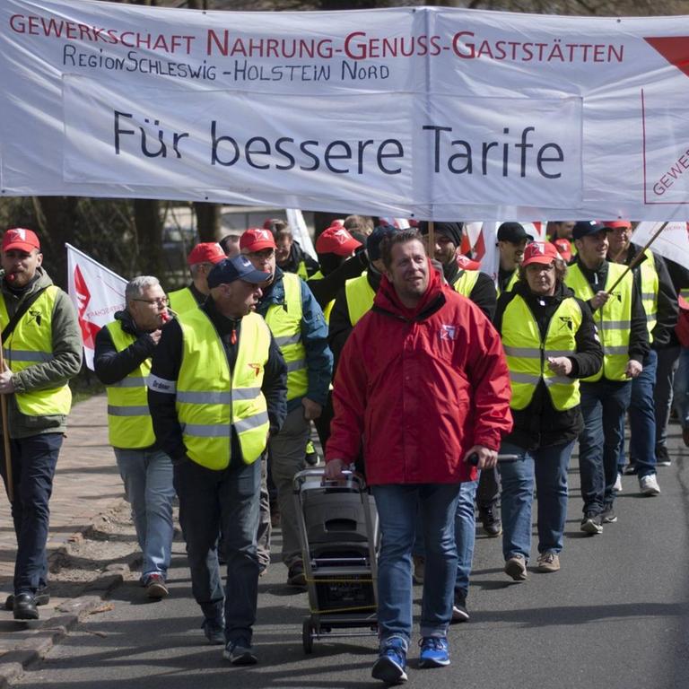 Mitarbeiter der Flensburger Brauerei halten während eines Warnstreiks Transparente mit der Forderung nach besseren Tarifen hoch