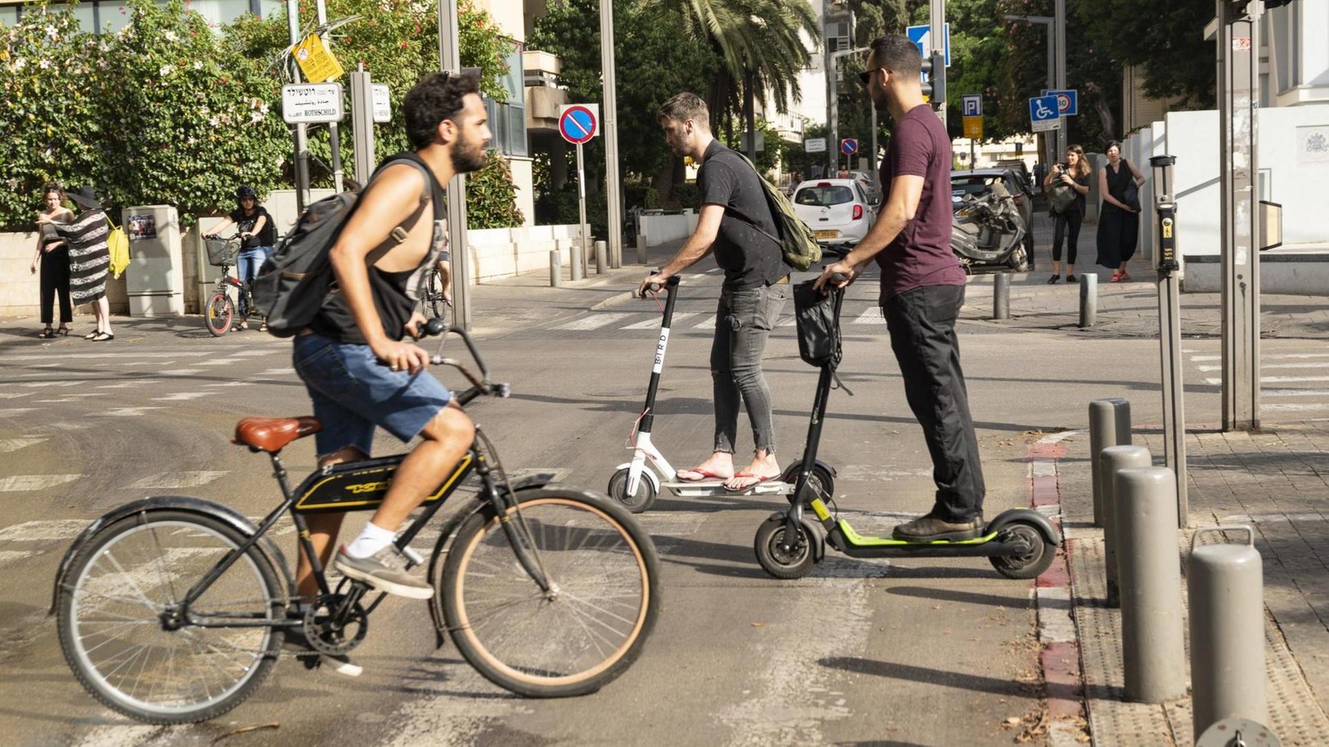 Fahrrad- und E-Rollerfahrer überqueren eine Straße in Tel Aviv.