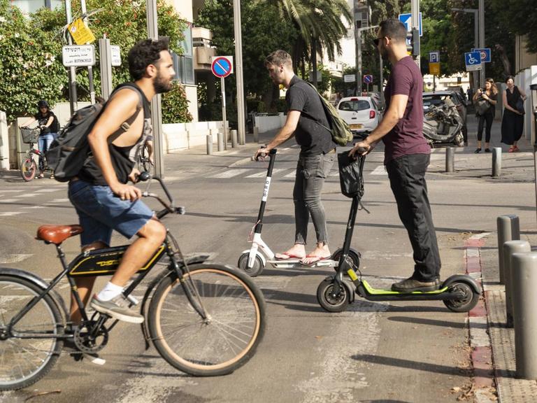 Fahrrad- und E-Rollerfahrer überqueren eine Straße in Tel Aviv.