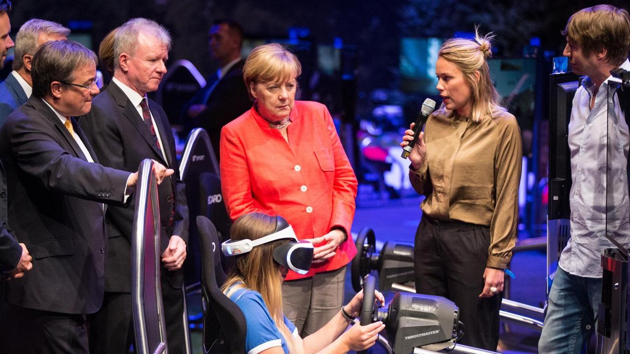 Bundeskanzlerin Angela Merkel schaut auf der Gamescom in Köln ein virtuelles Autorenn-Computerspiel an. Bundeskanzlerin Angela Merkel schaut auf der Gamescom in Köln ein virtuelles Autorenn-Computerspiel an.