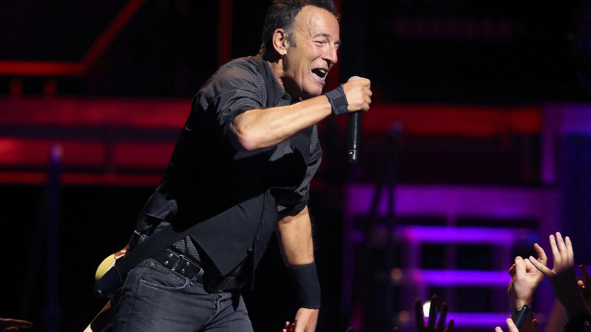 Bruce Springsteen singt bei einem Auftritt 2016 in Chicago auf der Bühne in ein Mikrofon. Hände recken sich ihm entgegen. Bruce Springsteen singt bei einem Auftritt 2016 in Chicago auf der Bühne in ein Mikrofon. Hände recken sich ihm entgegen.