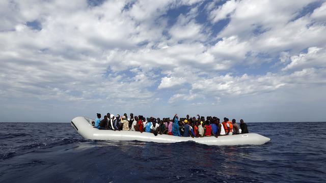 Vor der Insel Lampedusa warten Flüchtlinge in einem Schlauchboot darauf, in Sicherheit gebracht zu werden.