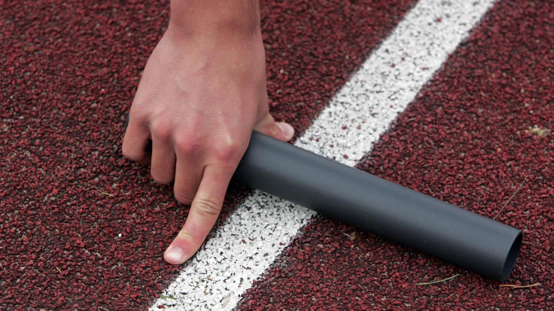 Ein Läufer von "Jugend trainiert für Olympia" einer 4x100m-Staffel hält einen Staffelstab in der Hand. Nahaufnahme der Hand, die den Stab hält, kurz vor dem Start. Ein Läufer von "Jugend trainiert für Olympia" einer 4x100m-Staffel hält einen Staffelstab in der Hand. Nahaufnahme der Hand, die den Stab hält, kurz vor dem Start.