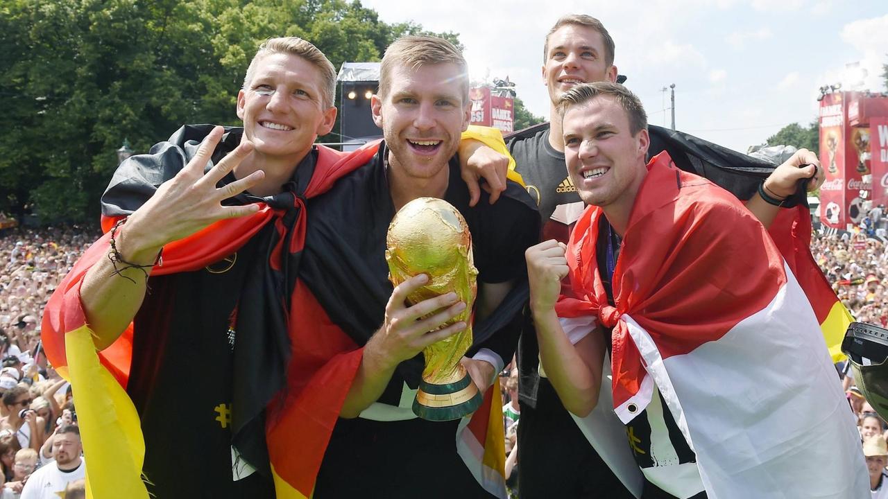 Auf der Fanmeile: v.l.: Bastian Schweinsteiger, Per Mertesacker, Torwart Manuel Neuer, Kevin Grosskreutz mit WM-Pokal und Deutschlandfahne Empfang der deutschen Fussball Nationalmannschaft auf der Fanmeile am Brandenburger Tor in Berlin. Auf der Fanmeile: v.l.: Bastian Schweinsteiger, Per Mertesacker, Torwart Manuel Neuer, Kevin Grosskreutz mit WM-Pokal und Deutschlandfahne Empfang der deutschen Fussball Nationalmannschaft auf der Fanmeile am Brandenburger Tor in Berlin.