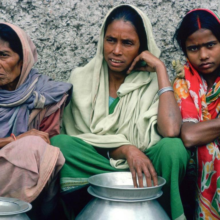 Drei Frauen und ein Baby in indischer Kleidung stehen für eine Essensspende an.