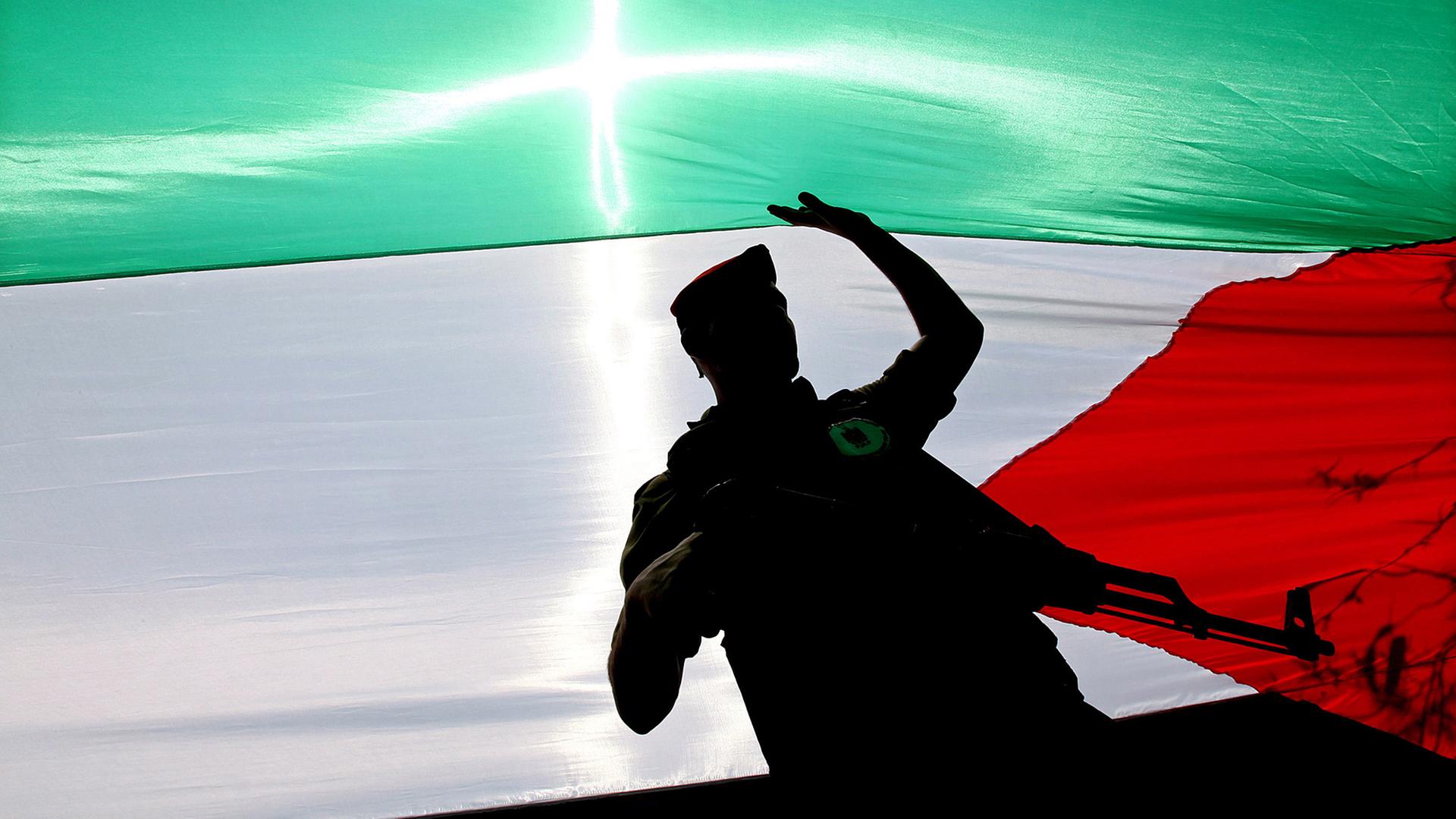 Ein bewaffneter Hamas-Aktivist läuft in Gaza-Stadt unter einer Palästinenser-Flagge. Ein bewaffneter Hamas-Aktivist läuft in Gaza-Stadt unter einer Palästinenser-Flagge.