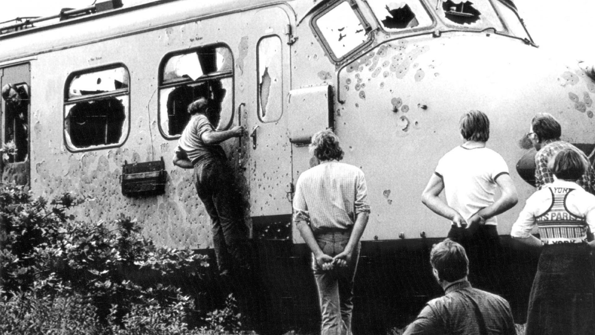 Schaulustige betrachten am 11 Juni 1977 nach Beendigung der Geiselnahme die beschädigte Lok. Am 23. Mai 1977 hatten süd-molukkische Terroristen einen Intercity bei Assen überfallen und 55 Menschen in ihre Gewalt gebracht. Gleichzeitig überfiel eine weitere Gruppe Südmolukker die Grundschule von Bovensmilde und nimmt 120 Kinder und fünf Lehrer als Geiseln. Die Terroristen, die für die Unabhängigkeit ihres Landes von Indonesien kämpfen, forderten die Freilassung von 21 in Holland inhaftierten Landsleuten und ein Flugzeug. Nach dem Scheitern mehrerer Vermittlungsversuche und der Freilassung der Schulkinder und weiterer Geiseln stürmt am 11.6.1977 eine Elite-Einheit der niederländischen Streitkräfte den Zug und befreit die verbliebenen 51 Geiseln. Zwei Geiseln und sechs der neun Terroristen werden dabei getötet. Ohne Bluvergießen werden die vier in der Schule verbliebenen Lehrer befreit. | Schaulustige betrachten am 11 Juni 1977 nach Beendigung der Geiselnahme die beschädigte Lok. Am 23. Mai 1977 hatten süd-molukkische Terroristen einen Intercity bei Assen überfallen und 55 Menschen in ihre Gewalt gebracht. Gleichzeitig überfiel eine weitere Gruppe Südmolukker die Grundschule von Bovensmilde und nimmt 120 Kinder und fünf Lehrer als Geiseln. Die Terroristen, die für die Unabhängigkeit ihres Landes von Indonesien kämpfen, forderten die Freilassung von 21 in Holland inhaftierten Landsleuten und ein Flugzeug. Nach dem Scheitern mehrerer Vermittlungsversuche und der Freilassung der Schulkinder und weiterer Geiseln stürmt am 11.6.1977 eine Elite-Einheit der niederländischen Streitkräfte den Zug und befreit die verbliebenen 51 Geiseln. Zwei Geiseln und sechs der neun Terroristen werden dabei getötet. Ohne Bluvergießen werden die vier in der Schule verbliebenen Lehrer befreit. |