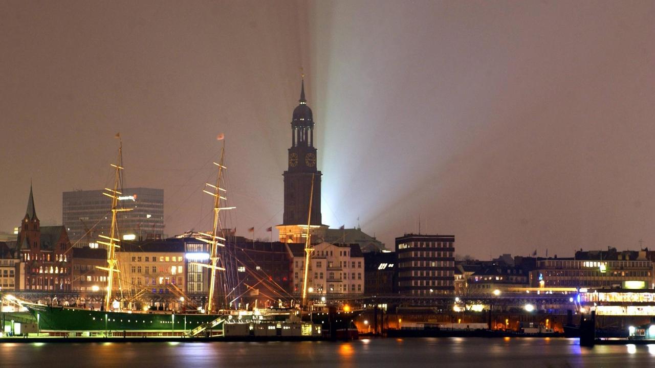 Der Hamburger Hafen erstrahlt in der Nachtbeleuchtung, im Hintergrund ragt der Turm des Kirche laserstrahlend hervor. Der Hamburger Hafen erstrahlt in der Nachtbeleuchtung, im Hintergrund ragt der Turm des Kirche laserstrahlend hervor.