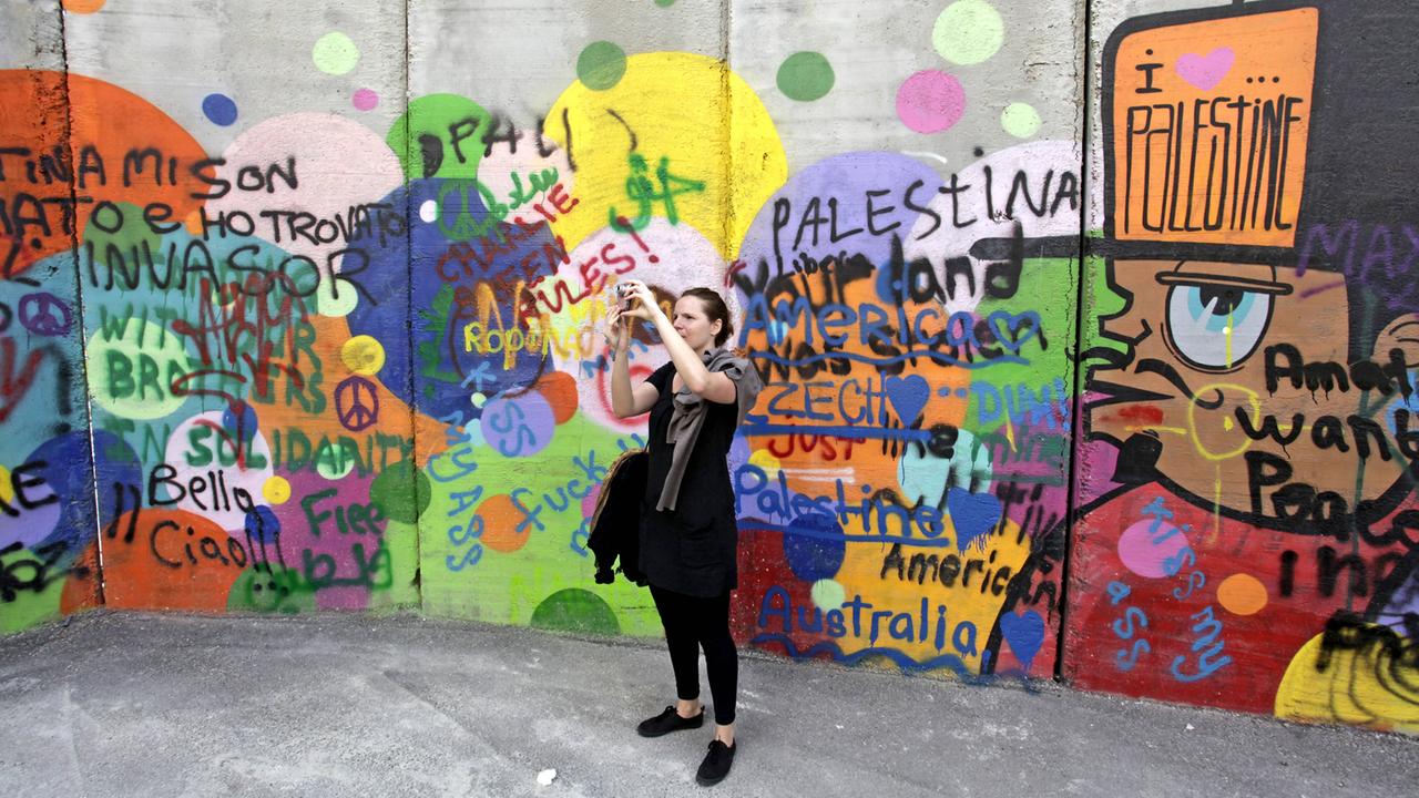 Eine junge Frau macht auf der palästinensischen Seite der Sperrmauer zwischen Bethlehem, Westjordanland und Jerusalem ein Foto. Eine junge Frau macht auf der palästinensischen Seite der Sperrmauer zwischen Bethlehem, Westjordanland und Jerusalem ein Foto.