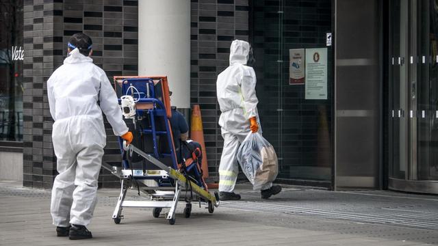 Zwei Krankenpfleger in Schutzkleidung auf dem Weg ins Karolinska Institut Stockholm mit einem Patienten