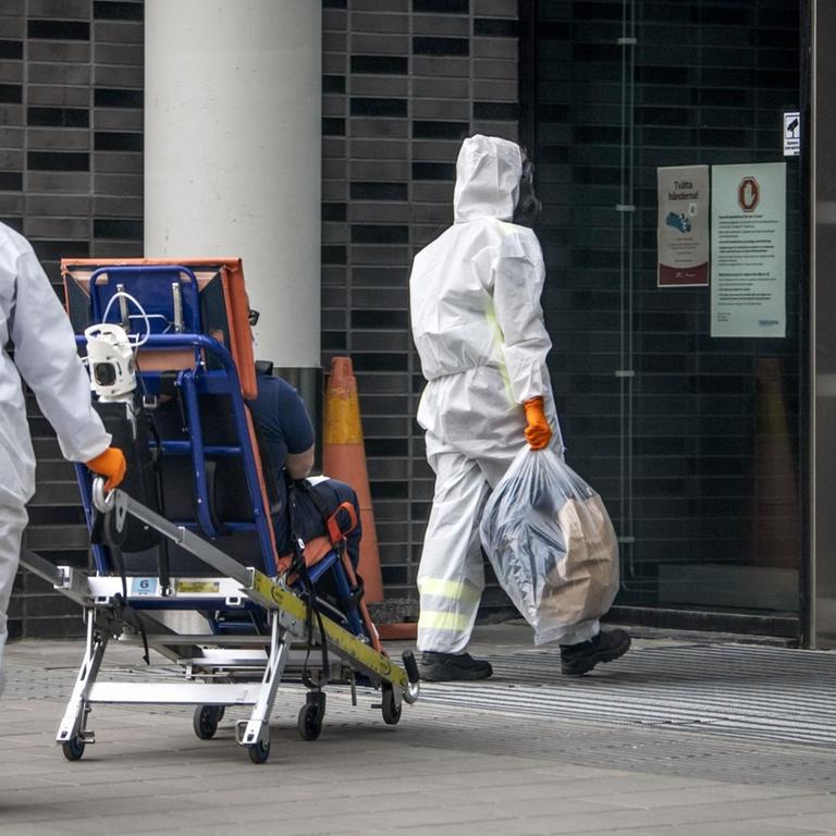 Zwei Krankenpfleger in Schutzkleidung auf dem Weg ins Karolinska Institut Stockholm mit einem Patienten