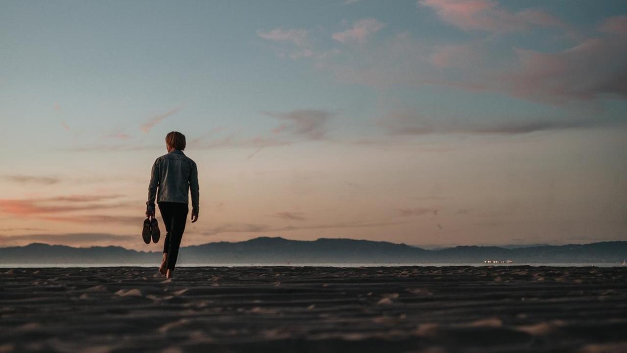 Ein Mann geht barfuß einen Strand entlang. Ein Mann geht barfuß einen Strand entlang.