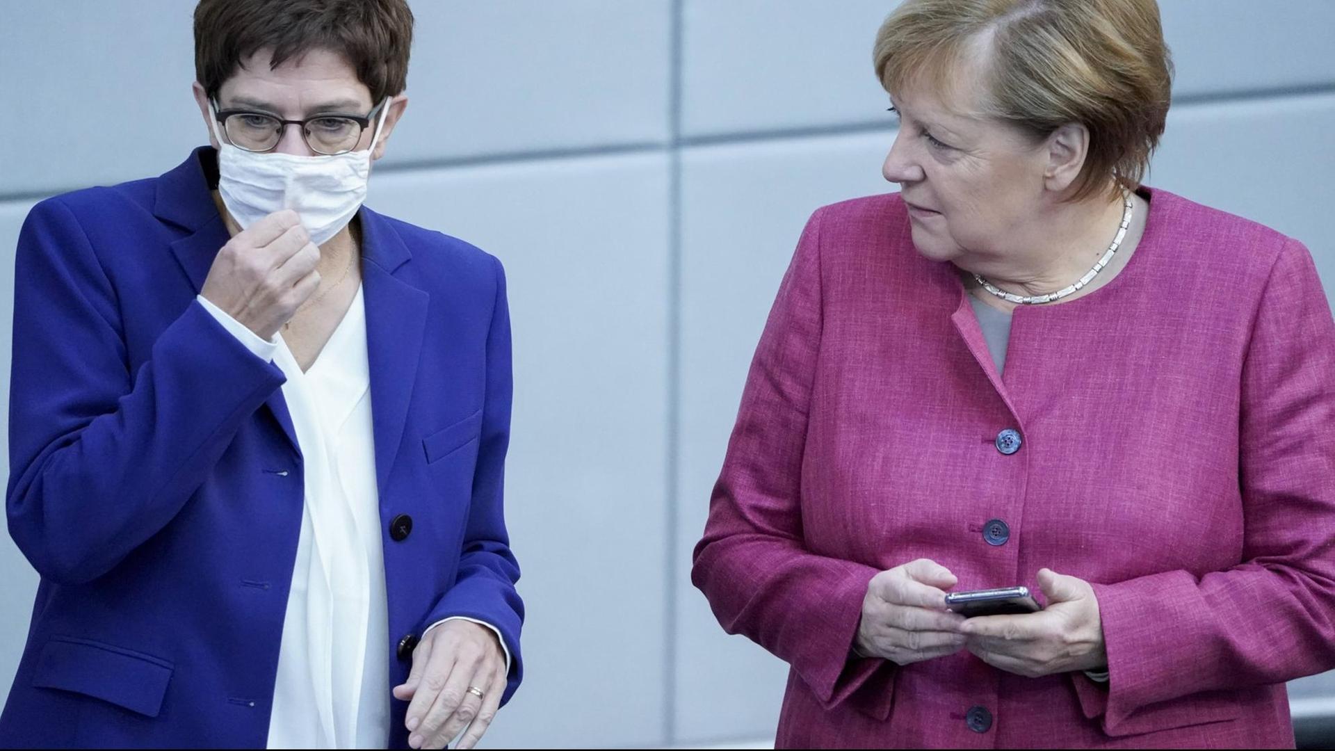 Annegret Kramp-Karrenbauer mit Mund-Nasenschutz, rechts neben ihr Bundeslkanzlerin Angela Merkel mit einem Handy in der Hand Annegret Kramp-Karrenbauer mit Mund-Nasenschutz, rechts neben ihr Bundeslkanzlerin Angela Merkel mit einem Handy in der Hand
