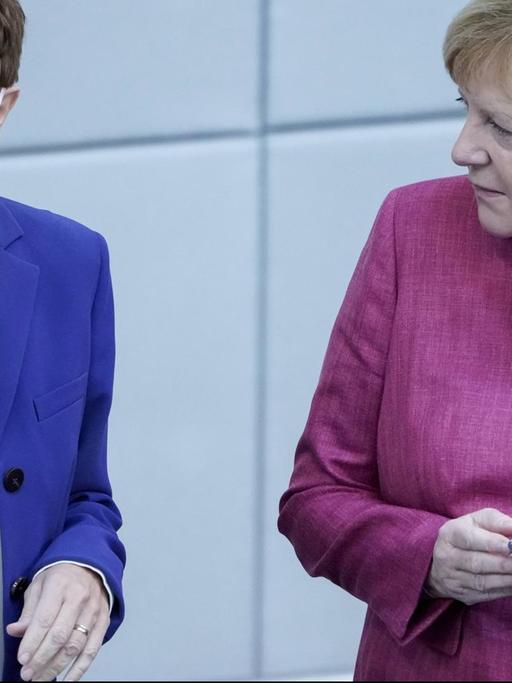 Annegret Kramp-Karrenbauer mit Mund-Nasenschutz, rechts neben ihr Bundeslkanzlerin Angela Merkel mit einem Handy in der Hand