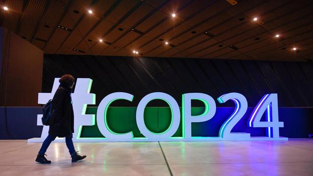 Eine Frau geht vor einem beleuchteten Schriftzug "#COP24" entlang