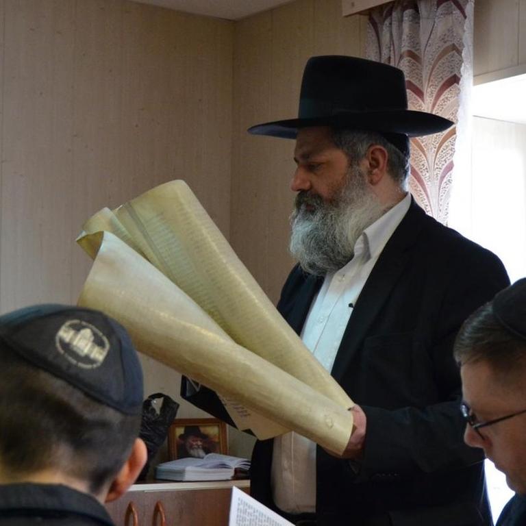 Rabbiner Ifrah Abramow steht am Tisch und hält Papierrollen