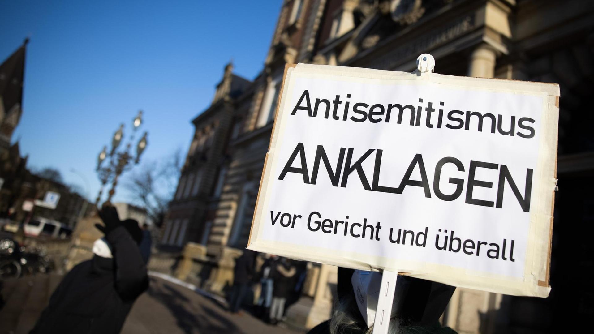 Eine Teilnehmerin einer Kundgebung hält ein Schild mit dem Text "Antisemitismus Anklagen vor Gericht und überall" vor dem Strafjustizgebäude in Hamburg. Dort begann gut vier Monate nach dem Angriff auf einen jüdischen Studenten vor der Hamburger Synagoge der Prozess gegen den mutmaßlichen Täter. Eine Teilnehmerin einer Kundgebung hält ein Schild mit dem Text "Antisemitismus Anklagen vor Gericht und überall" vor dem Strafjustizgebäude in Hamburg. Dort begann gut vier Monate nach dem Angriff auf einen jüdischen Studenten vor der Hamburger Synagoge der Prozess gegen den mutmaßlichen Täter.