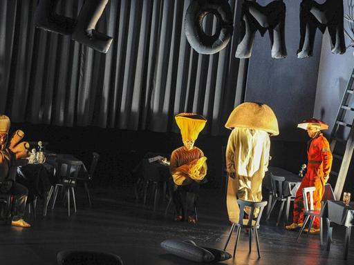 Vier Schauspieler in Gelb als Hand und Stehlampen kostümiert stehen unter dem Schriftzug "Willkommen".