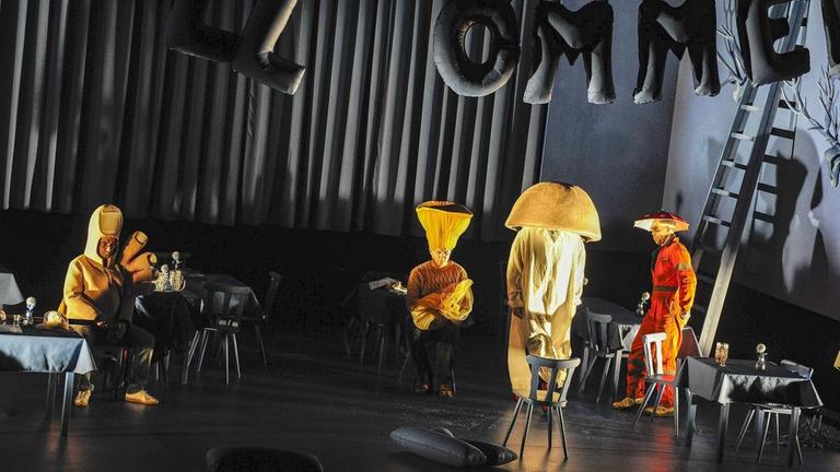 Vier Schauspieler in Gelb als Hand und Stehlampen kostümiert stehen unter dem Schriftzug "Willkommen". Vier Schauspieler in Gelb als Hand und Stehlampen kostümiert stehen unter dem Schriftzug "Willkommen".