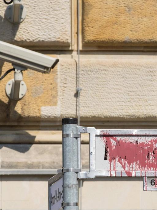 Im Bild ist das mit rote Farbe besprühte Straßenschild Mohrenstraße zu sehen. Darüber hängt an einer Hauswand eine Überwachungskamera.
