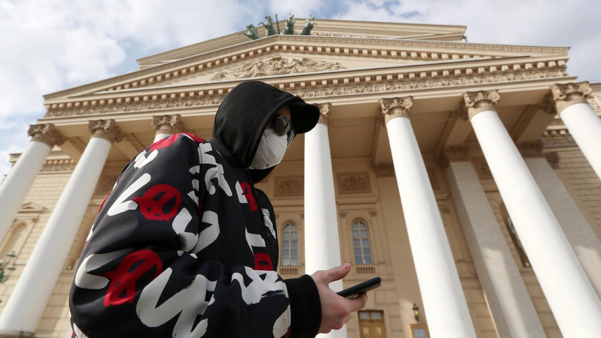 Ein Mann mit Smartphone, Mundschutz und Kapuzenpullover vor dem Bolshoi Theater in Moskau. Ein Mann mit Smartphone, Mundschutz und Kapuzenpullover vor dem Bolshoi Theater in Moskau.
