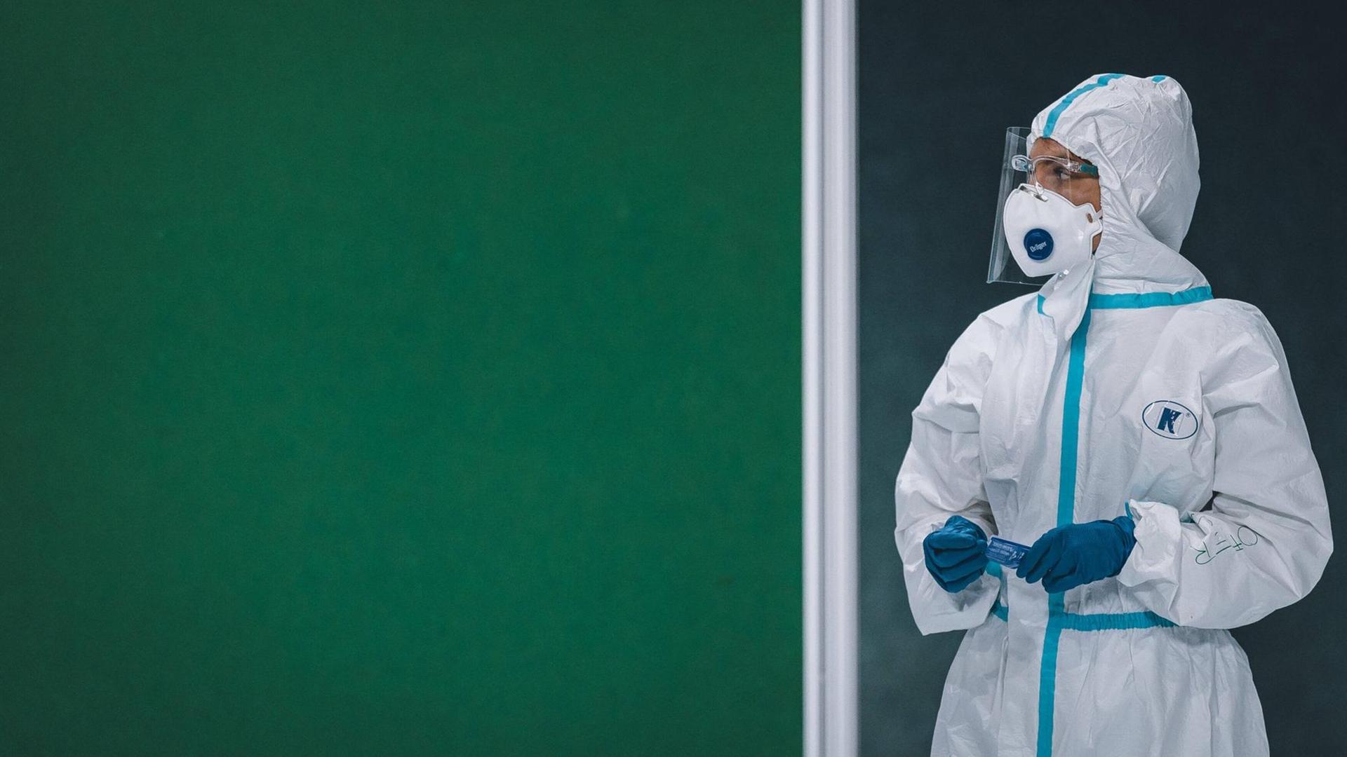Eine Frau in einem Schutzanzug steht am 05.12.2020 in einer Coronvirus-Teststation in Saalfelden, Österreich, vor einer grünen Wand Eine Frau in einem Schutzanzug steht am 05.12.2020 in einer Coronvirus-Teststation in Saalfelden, Österreich, vor einer grünen Wand
