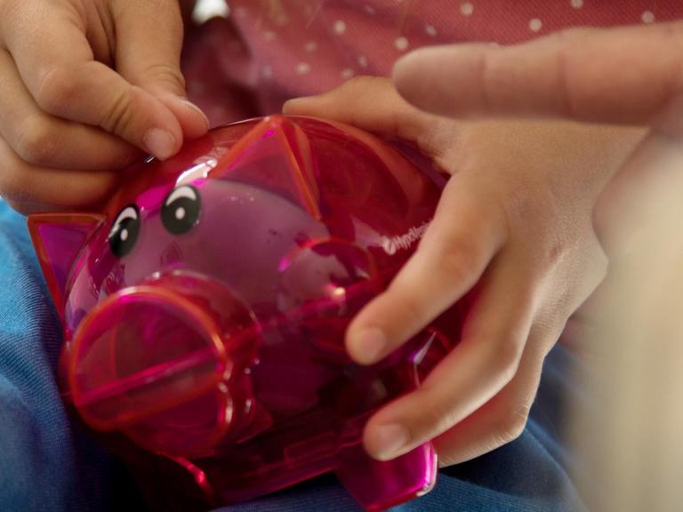 Ein kleines Mädchen steckt eine Münze in ihr Sparschwein.