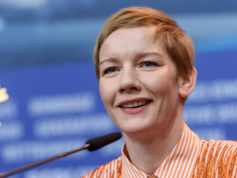 Schauspielerin Sandra Hüller mit kurzen Haaren, schaut bei der Pressekonferenz der Internationalen Jury anlässlich der 69. Internationalen Filmfestspiele in die Kamera. Im Hintergrund das Berlinale Logo, ein goldener Bär.