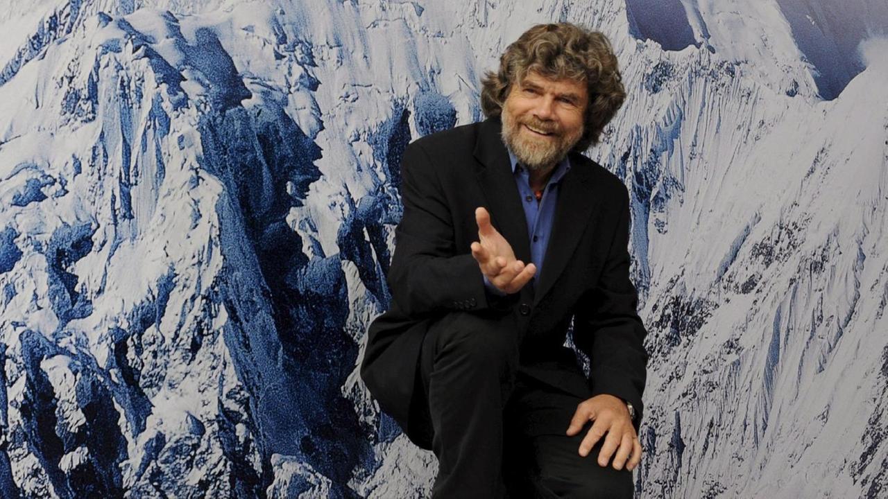 Reinhold Messner vor einer Fototapete, die schneebedeckte Berggipfel zeigt. Reinhold Messner vor einer Fototapete, die schneebedeckte Berggipfel zeigt.