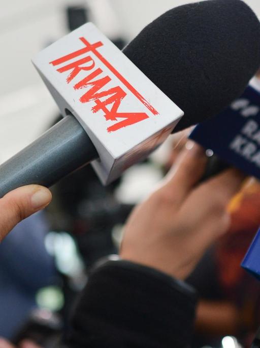Zahlreiche Mikrofone werden von Journalisten gehalten.