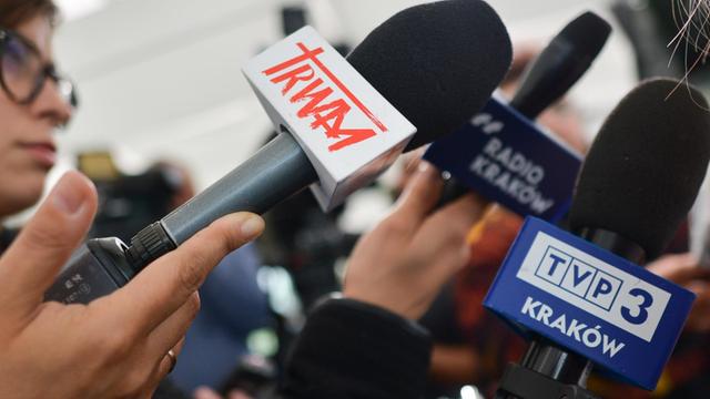 Zahlreiche Mikrofone werden von Journalisten gehalten.