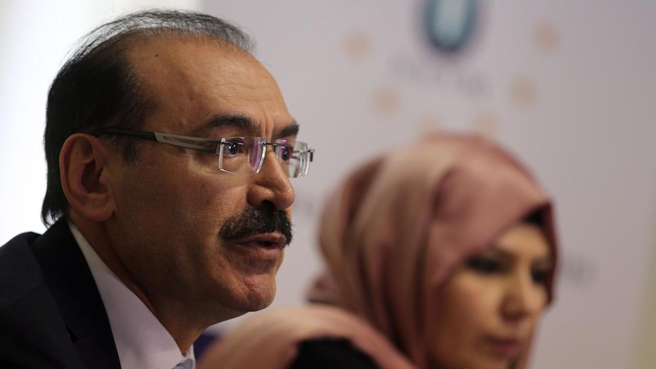 Süleyman Celik, ehemaliger Vorsitzender der Union europäisch-türkischer Demokraten, sprechend, im Hintergrund unscharf sitzt eine Frau mit Kopftuch Süleyman Celik, ehemaliger Vorsitzender der Union europäisch-türkischer Demokraten, sprechend, im Hintergrund unscharf sitzt eine Frau mit Kopftuch