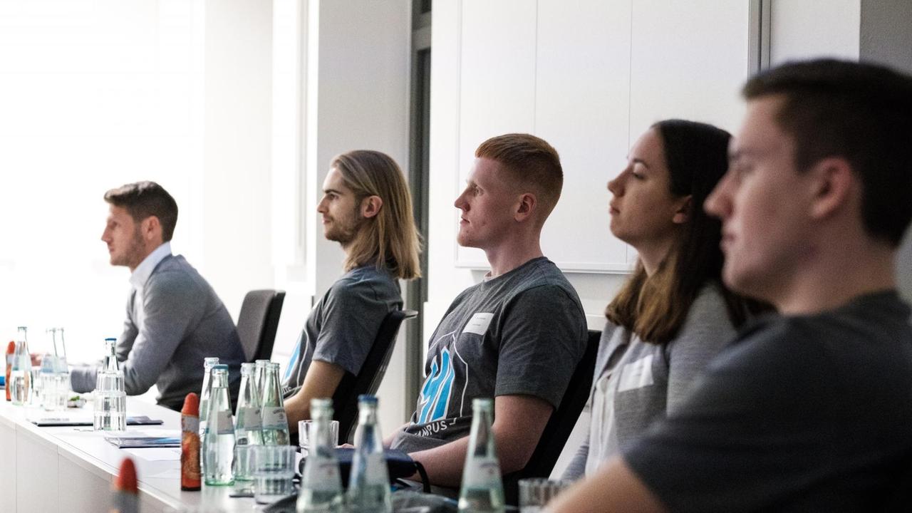 Junge Trainer und Trainerinnen sitzen an einem langen Tisch und hören einem Vortrag zu. Junge Trainer und Trainerinnen sitzen an einem langen Tisch und hören einem Vortrag zu.