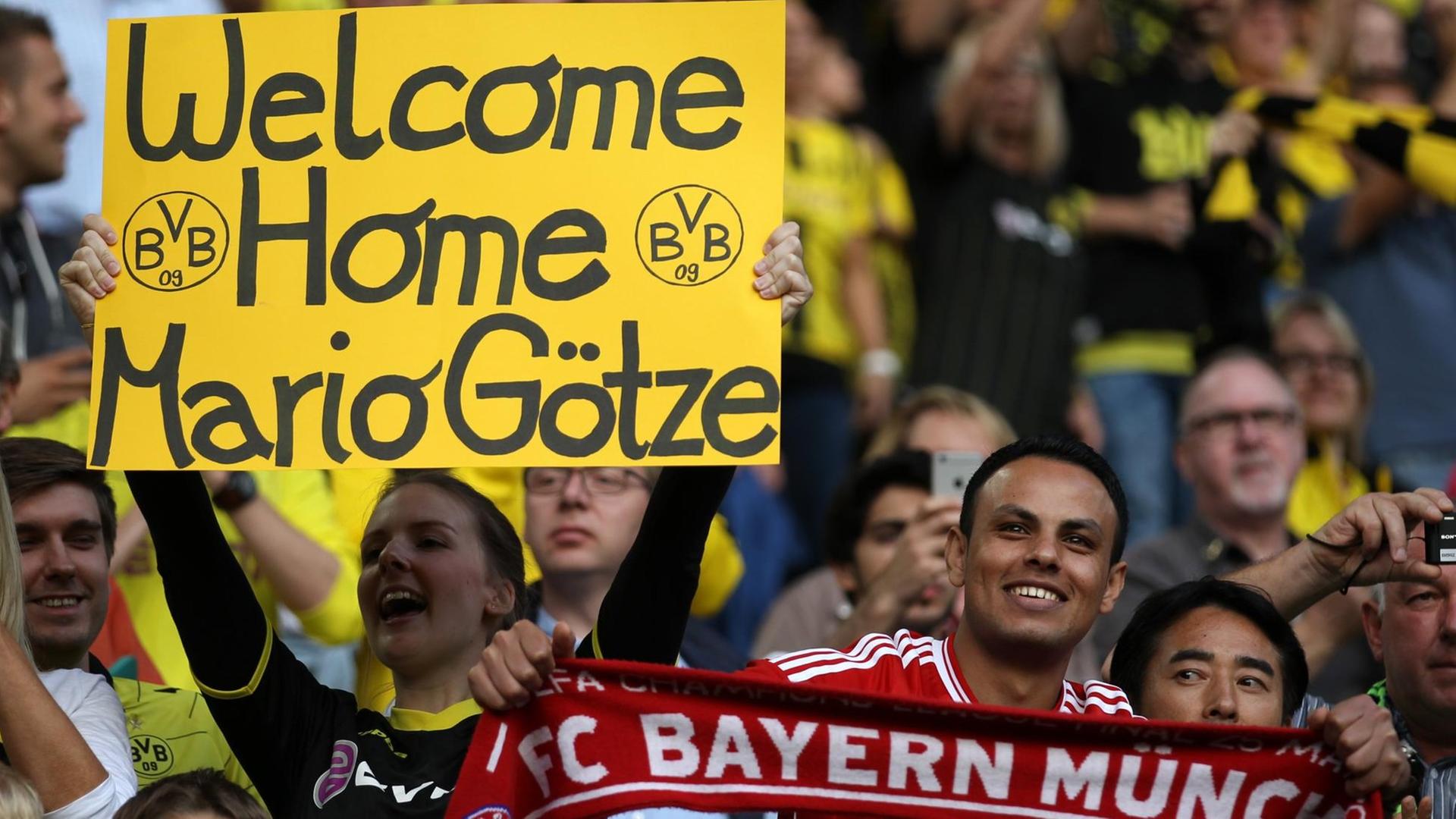 Ein Fan von Dortmund hält ein Schild mit der Aufschrift "Welcome Home Mario Götze" hoch. Rechts ein Fan von Bayern München. Ein Fan von Dortmund hält ein Schild mit der Aufschrift "Welcome Home Mario Götze" hoch. Rechts ein Fan von Bayern München.