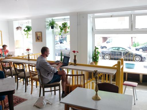 Im Café be`kech sitzen Gäste vor Tischen.