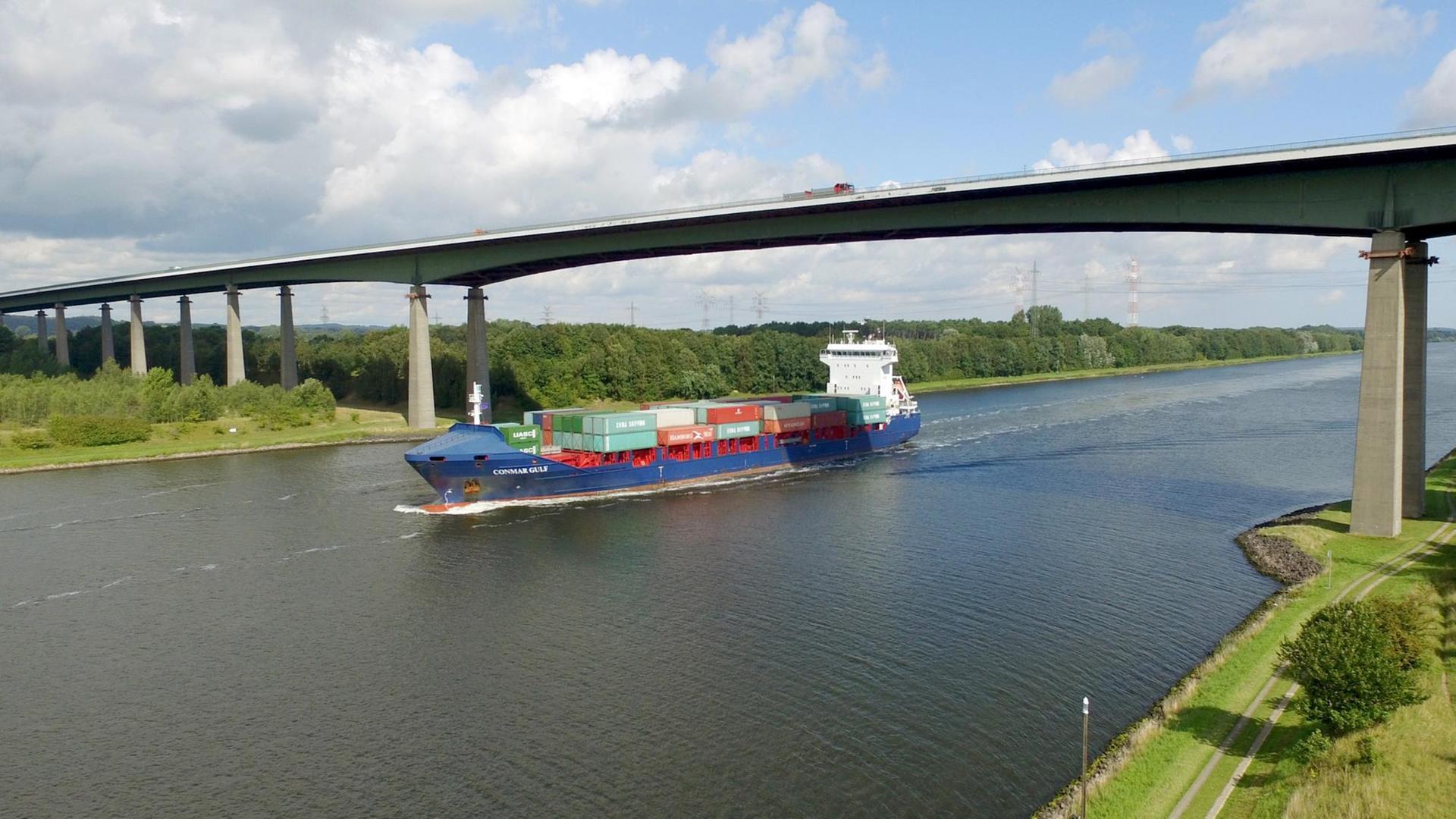 Ein Containerschiff fährt am 03.09.2015 auf dem Nord-Ostsee-Kanal in Höhe der Rader Hochbrücke der Autobahn 7 bei Rendsburg (Schleswig-Holstein). Foto: Carsten Rehder | Verwendung weltweit Ein Containerschiff fährt am 03.09.2015 auf dem Nord-Ostsee-Kanal in Höhe der Rader Hochbrücke der Autobahn 7 bei Rendsburg (Schleswig-Holstein). Foto: Carsten Rehder | Verwendung weltweit