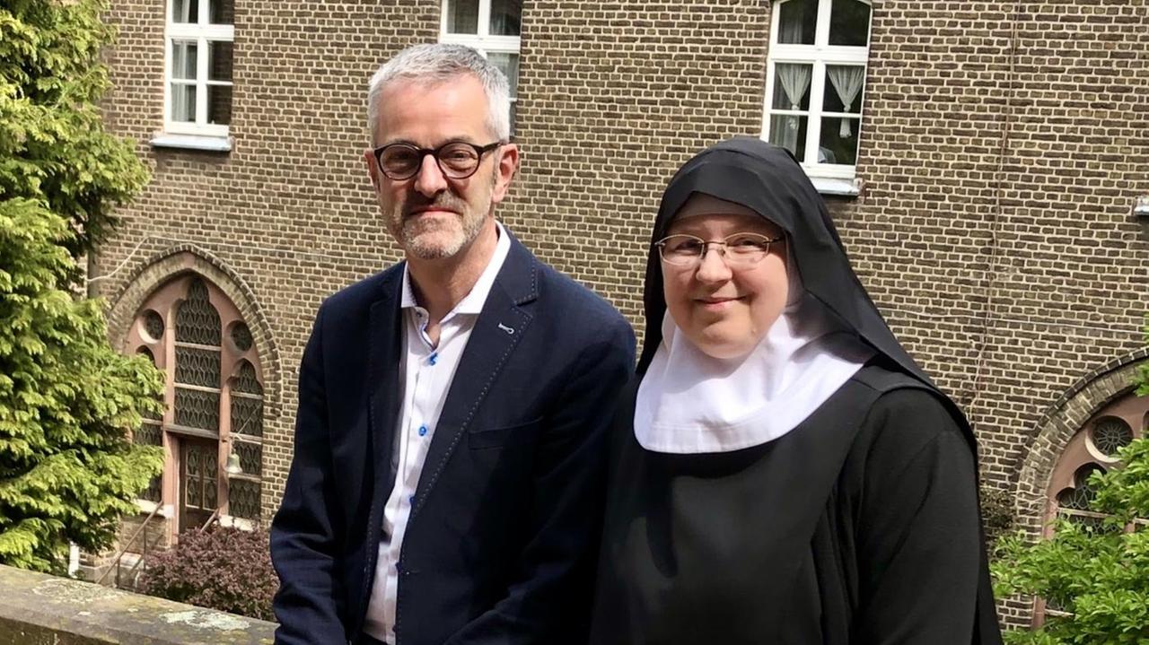 Thomas Frings und Emmanuela Kohlhaas, er im Anzug, sie im Habit, sitzen auf der Klostermauer in der Sonne Thomas Frings und Emmanuela Kohlhaas, er im Anzug, sie im Habit, sitzen auf der Klostermauer in der Sonne