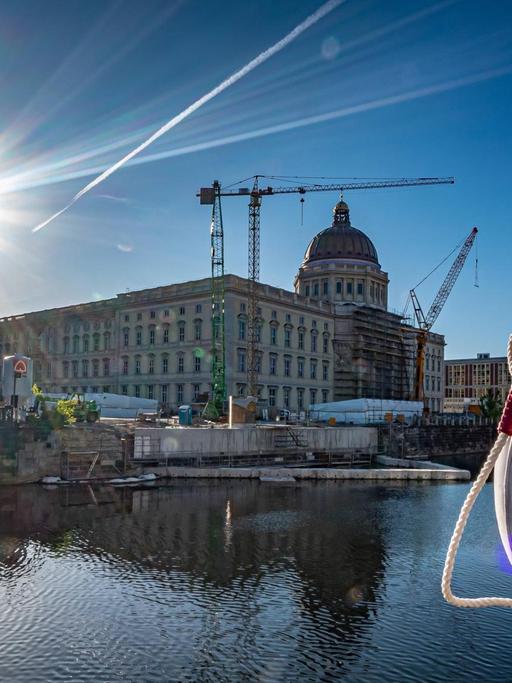 Blick auf das Humboldt Forum Berlin am Schlossplatz gegen die Sonne, im Vordergrund ein Rettungsreifen und die Spree