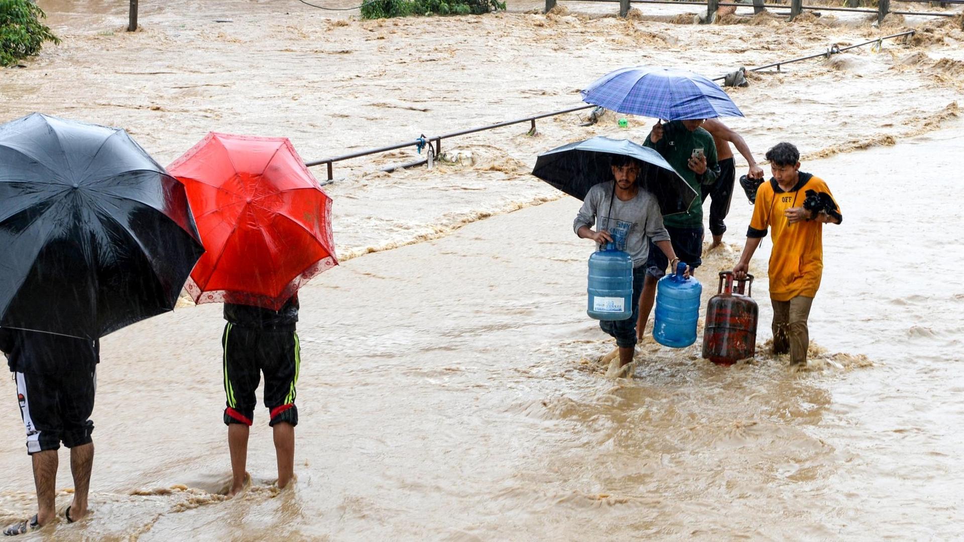 Anwohner laufen mit Regenschirmen durch einen überfluteten Teil von Kathmandu.