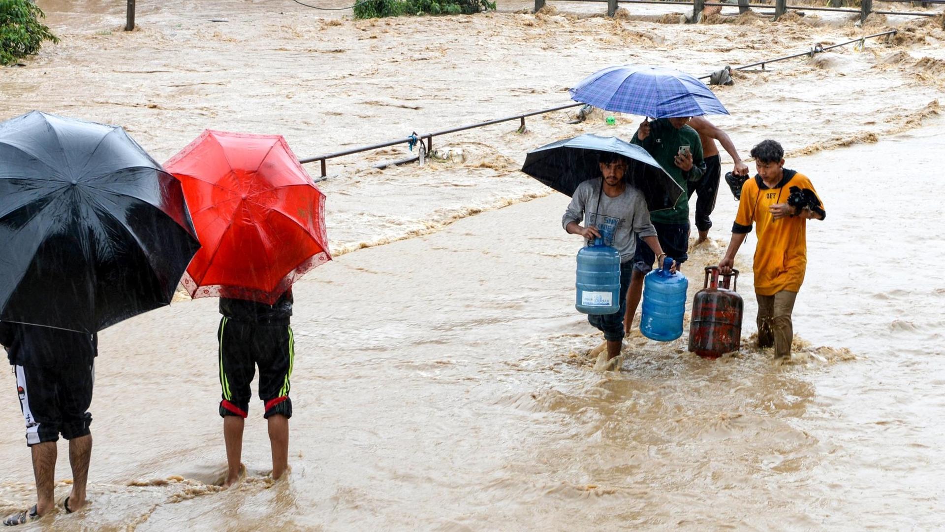 Anwohner laufen mit Regenschirmen durch einen überfluteten Teil von Kathmandu. Anwohner laufen mit Regenschirmen durch einen überfluteten Teil von Kathmandu.
