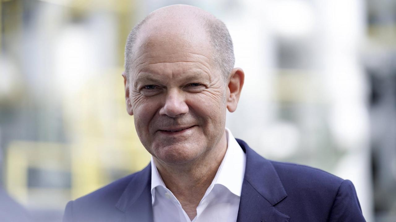 Olaf Scholz in dunkel-blauem Anzug und mit wenigen, sehr kurzen Haaren. Er schaut in die Kamera und lächelt. Olaf Scholz in dunkel-blauem Anzug und mit wenigen, sehr kurzen Haaren. Er schaut in die Kamera und lächelt.