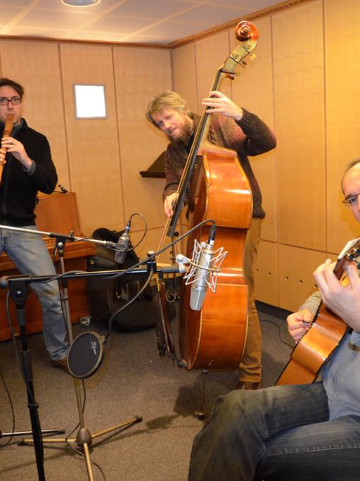 Auf dem Bild ist das Musiktrio "Wildes Holz" zu sehen: Tobias Reisige (links mit Mütze) auf der Flöte, in der Mitte Markus Conrads am Kontrabass und rechts (sitzend) Anto Karaula an der Gitarre.