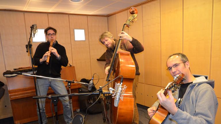 Auf dem Bild ist das Musiktrio "Wildes Holz" zu sehen: Tobias Reisige (links mit Mütze) auf der Flöte, in der Mitte Markus Conrads am Kontrabass und rechts (sitzend) Anto Karaula an der Gitarre. Auf dem Bild ist das Musiktrio "Wildes Holz" zu sehen: Tobias Reisige (links mit Mütze) auf der Flöte, in der Mitte Markus Conrads am Kontrabass und rechts (sitzend) Anto Karaula an der Gitarre.