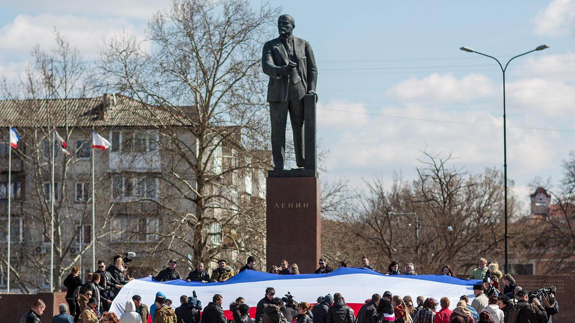 Dutzende Menschen halten am 18.03.2014 in Simferopol (Ukraine) anlässlich der Rede von Russlands Präsidenten Putin eine große russische Flagge vor dem Lenin-Denkmal in Händen. Dutzende Menschen halten am 18.03.2014 in Simferopol (Ukraine) anlässlich der Rede von Russlands Präsidenten Putin eine große russische Flagge vor dem Lenin-Denkmal in Händen.