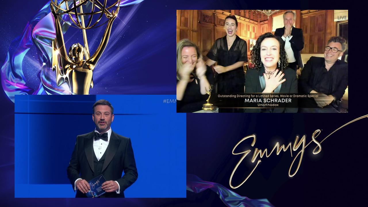 Die Emmy-Preisverleihung: Ein Mann im Anzug steht auf einer Bühne. Im Hintergrund ist eine Videoschalte eingeblendet, in der Maria Schrader sich über ihre Auszeichnung freut.