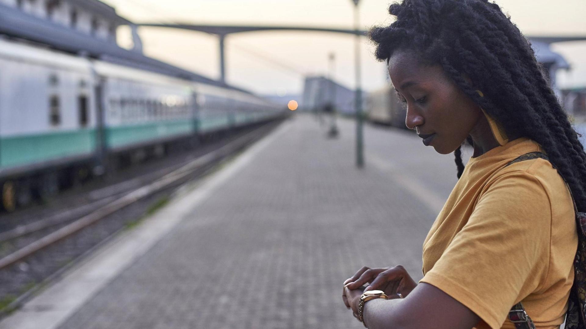 Eine junge Frau steht an einem Bahngleis und schaut auf die Uhr Eine junge Frau steht an einem Bahngleis und schaut auf die Uhr