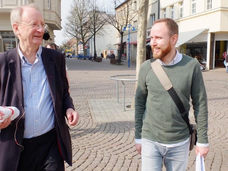 Klaus Staeck und Moderator Olaf Kosert schlendern über den Marktplatz von Bitterfeld.