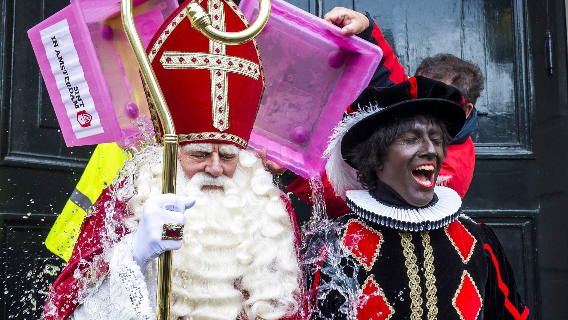 Zwei Darsteller sind verkleidet als Nikolaus mit weißem Bart, roter Bischofsmütze und Mitra und als Zwarter Piet mit schwarz angemaltem Gesicht in einem schwarzem Kostüm mit Karos.