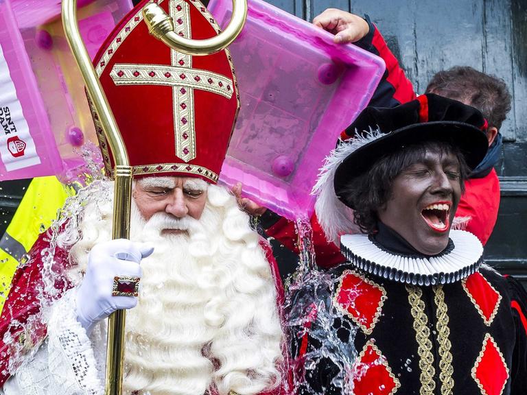 Zwei Darsteller sind verkleidet als Nikolaus mit weißem Bart, roter Bischofsmütze und Mitra und als Zwarter Piet mit schwarz angemaltem Gesicht in einem schwarzem Kostüm mit Karos.
